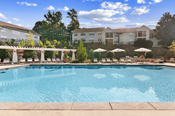 a swimming pool with lounge chairs and umbrellas in front of a building at Caveness Farms Apartments, North Carolina, 27587